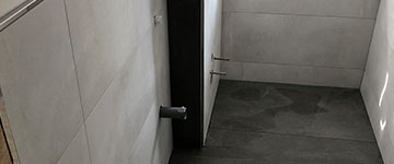 Linke Seite eines Badezimmers mit weißen Wandfliesen und grauen Bodenfliesen von BekOli Fliesenverlegung